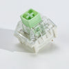 A close-up view of a light green tactile clicky mechanical keyboard switch with a clear plastic housing.