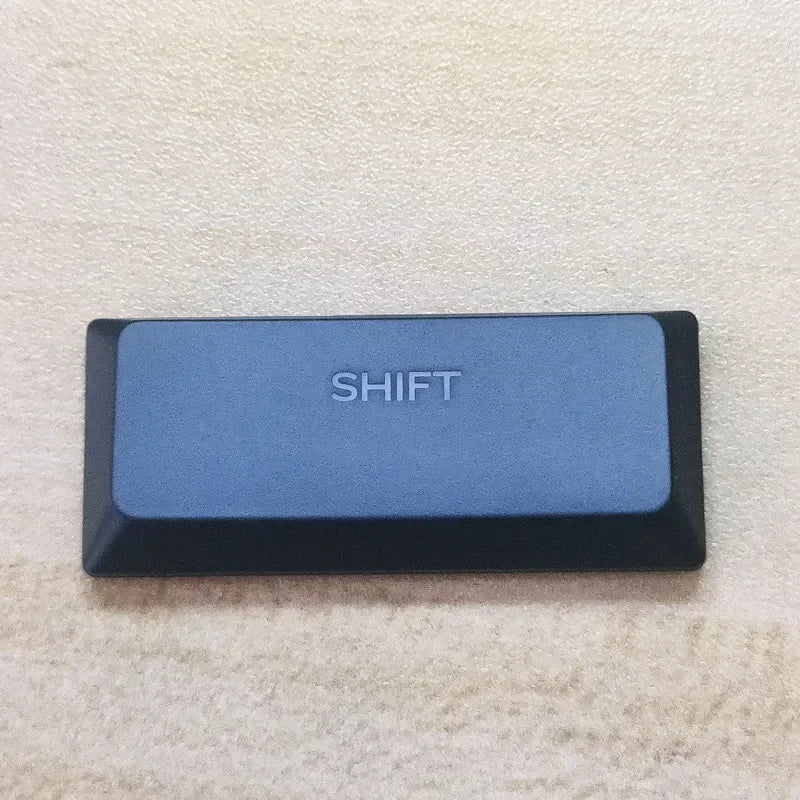 A rectangular blue keycap labeled SHIFT resting on a light beige surface.