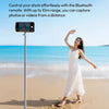 A woman stands on a beach holding a white magnetic phone tripod with a Bluetooth remote.
