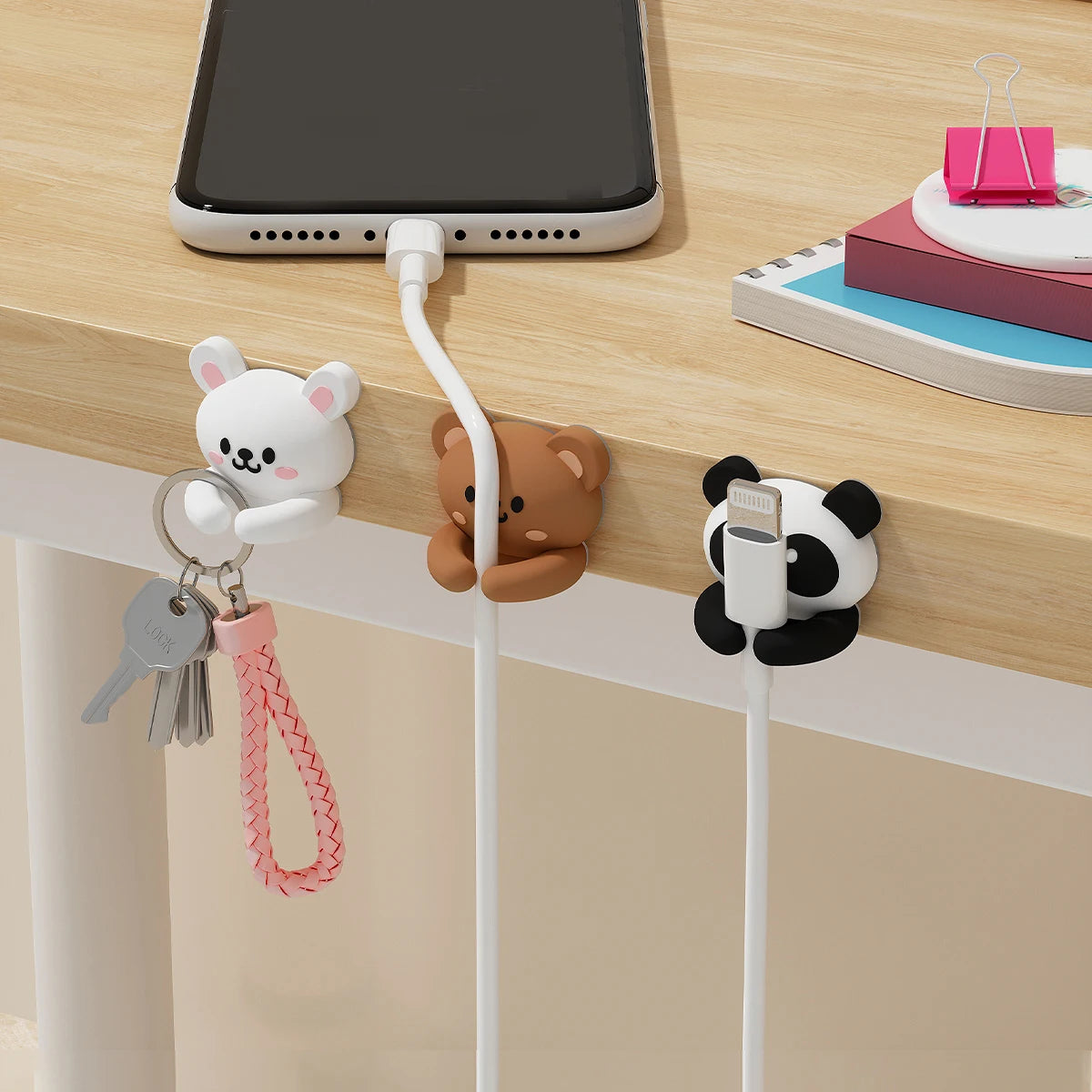 Cartoon desk cable organizers featuring animal-shaped holders for managing cords on a wooden surface.