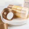 Rolls of satin ribbon in gold and beige colors displayed on a white surface.