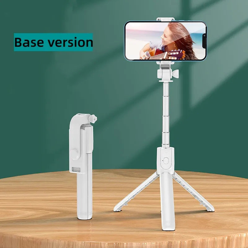 A white selfie stick tripod with a smartphone mounted, featuring a fill light and wireless remote, displayed on a wooden surf