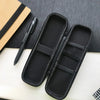 Black compact EVA hard shell pencil case with mesh pockets resting on a white surface next to a pen and notebook.