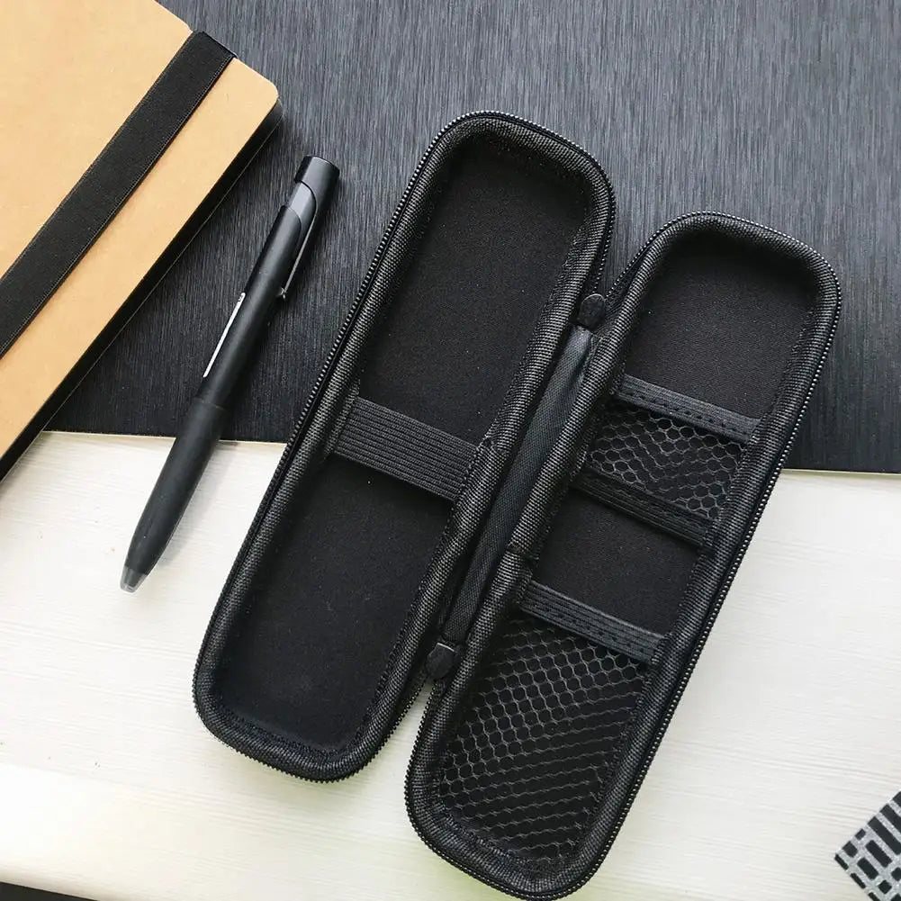 Black compact EVA hard shell pencil case with mesh pockets resting on a white surface next to a pen and notebook.