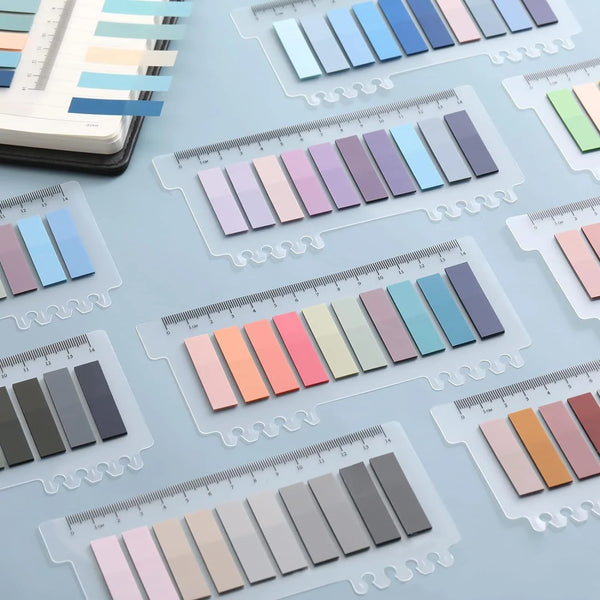 A collection of transparent self-adhesive sticky notes in various pastel and muted colors are displayed on a light blue surfa