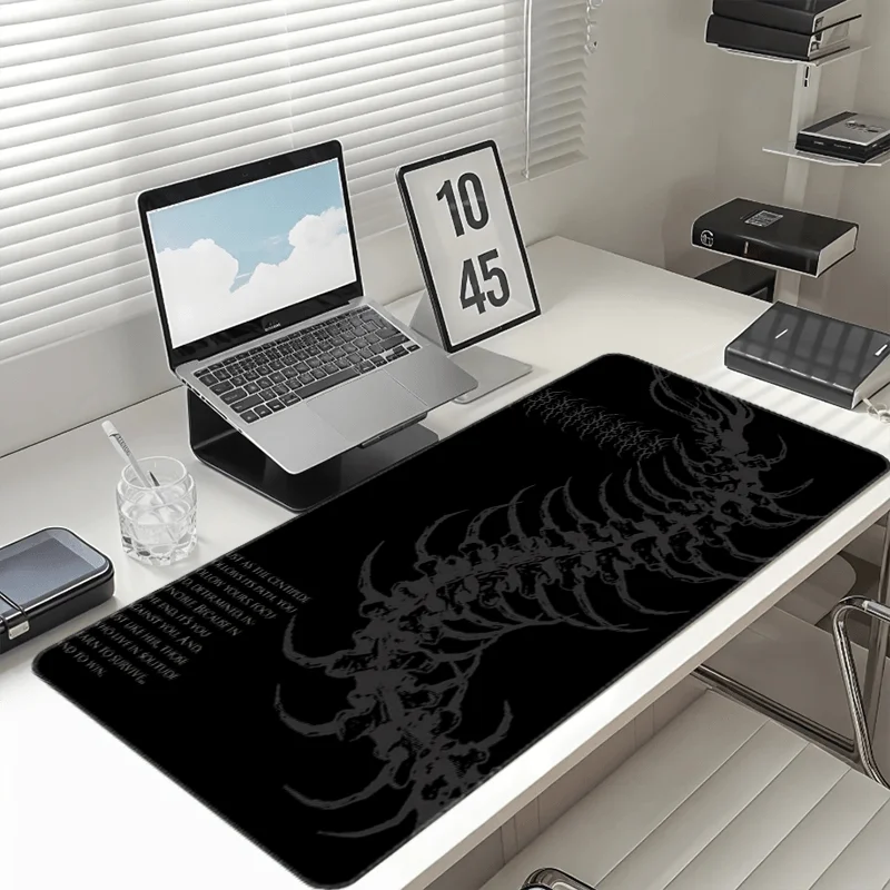 Black gaming mouse pad featuring a white gothic centipede design placed on a white desk next to a laptop.
