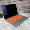 A silver silicone keyboard cover for a MacBook Air or Pro is displayed on a light wooden surface.
