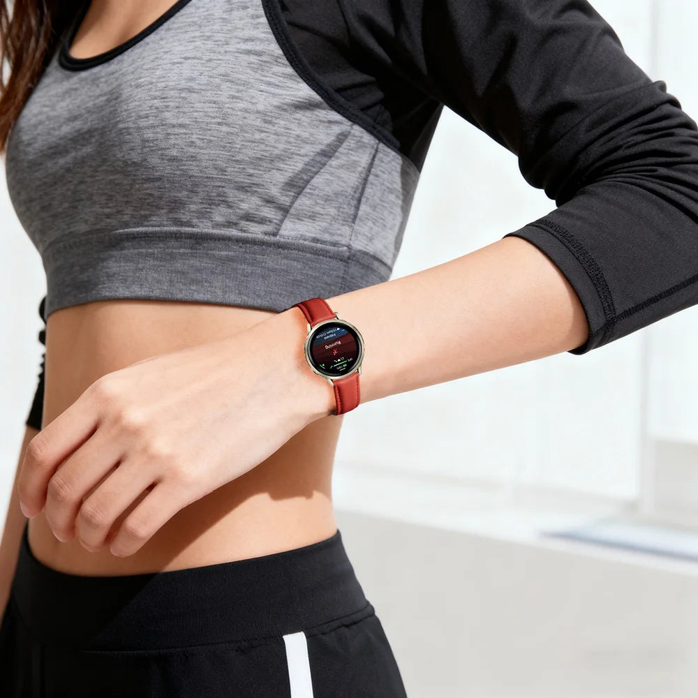 A close-up of a woman wearing a dark gray cropped top and a brown leather watch with quick release pins on her wrist.