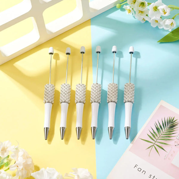 Five pearl beaded ballpoint pens displayed on a light blue and yellow background with white flowers.