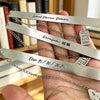 Hand holding several stainless steel bookmarks engraved with names and dates
