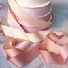 Stack of matte finish satin ribbon rolls in soft pink and peach tones