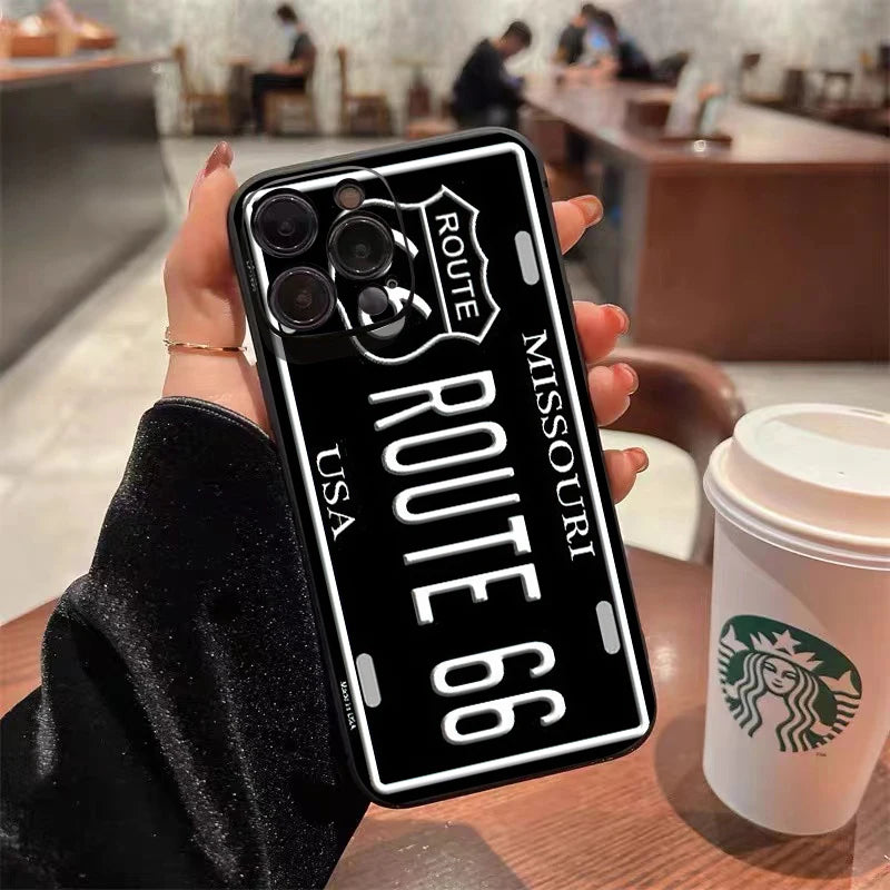 A hand holds a black phone case designed like a vintage license plate with the text Route 66 and USA.