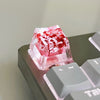 A translucent pink resin keycap featuring red botanical elements, resting on a dark keyboard surface.