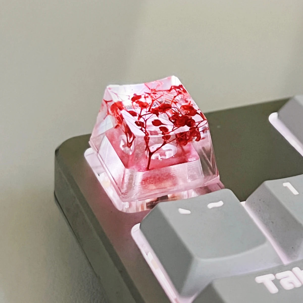 A translucent pink resin keycap featuring red botanical elements, resting on a dark keyboard surface.