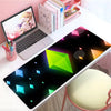 A large gaming mouse pad featuring a dark background with glowing green and blue geometric shapes on a white desk.
