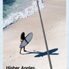 A selfie stick is positioned on a sandy beach, with a person surfing and the ocean in the background.