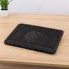 A black laptop cooling pad with an integrated fan is placed on a wooden desk next to a potted plant.