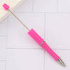 A pink DIY beadable pen with a gold-colored metal tip resting on a white surface.