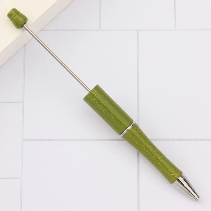 A green DIY beadable pen with a silver tip and cap resting on a white surface.