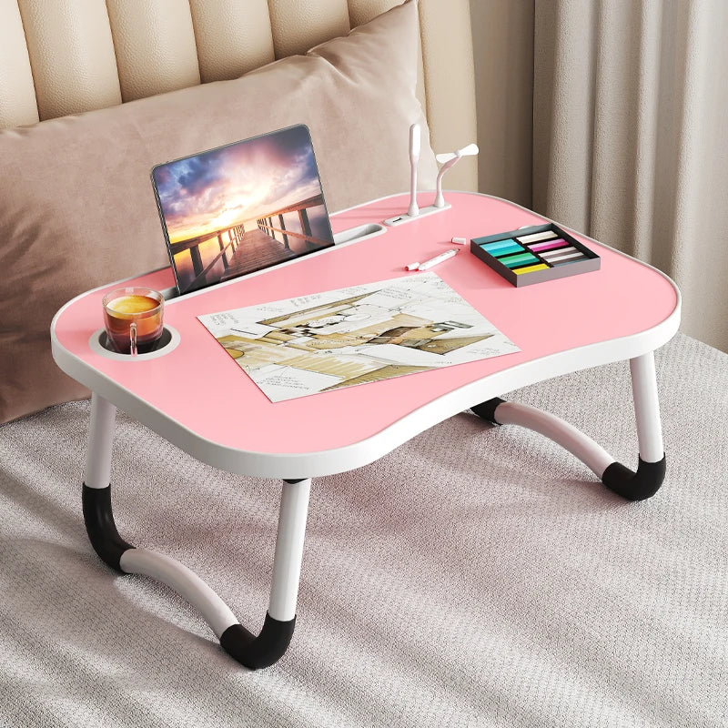 A pink multi-functional laptop desk organizer tray with a wooden laptop and art supplies on a light gray surface.