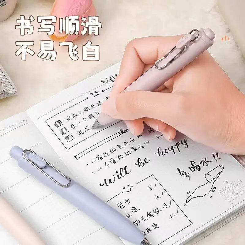 A hand holds a light purple Uni-Ball One Mini Cute Gel Pen writing on a spiral notebook.
