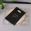 A black thank you gift bag with a handle is placed on top of newspaper print.