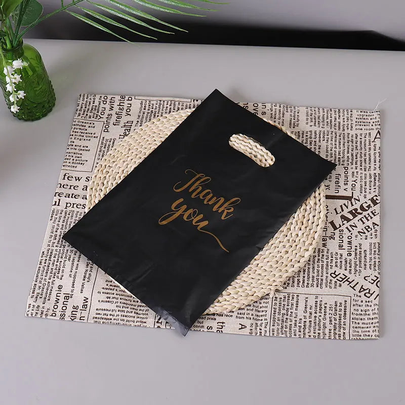A black thank you gift bag with a handle is placed on top of newspaper print.