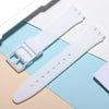 A white soft silicone watch strap is shown next to its replacement tools on a light blue and beige background.
