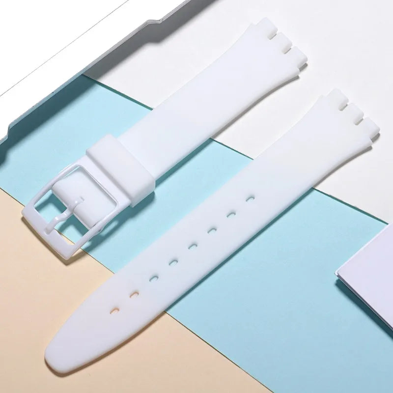A white soft silicone watch strap is shown next to its replacement tools on a light blue and beige background.