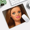 A close-up of a doll face design on a mouse pad with a white Apple-style mouse resting on it.