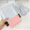 A hand holds a pink self-sealing plastic mailing bag, next to rolled white plastic bags.