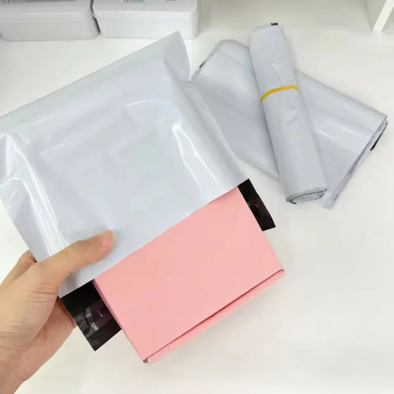 A hand holds a pink self-sealing plastic mailing bag, next to rolled white plastic bags.