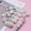 A collection of white and iridescent acrylic flower beads for jewelry making displayed on a pink background.