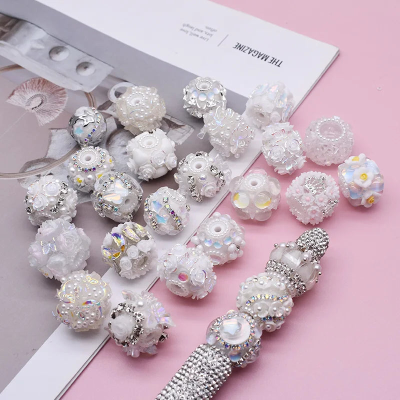 A collection of white and iridescent acrylic flower beads for jewelry making displayed on a pink background.