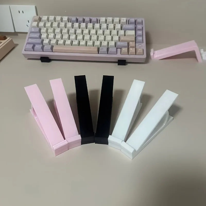 Two pink and white ergonomic keyboard riser stands with anti-slip bases are displayed on a light surface.