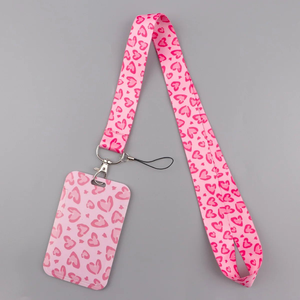 A pink heart-patterned lanyard with a tag is displayed against a gray background.