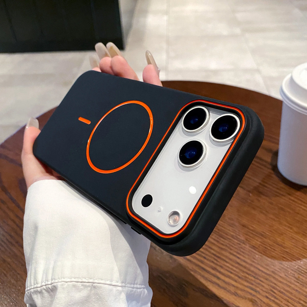 A hand holds a black magnetic wireless charging phone case with an orange charging indicator on a wooden surface.