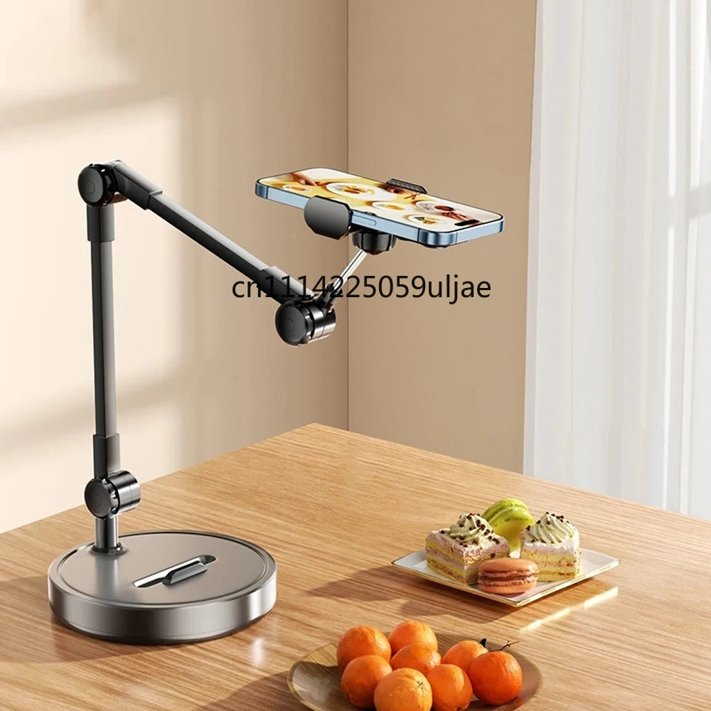 A black multi-angle adjustable phone holder stand is shown on a wooden table with fresh fruit nearby.
