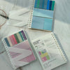 A stack of pastel sticky note notebooks and a colorful set of blue and teal sticky notes are displayed on a white surface.