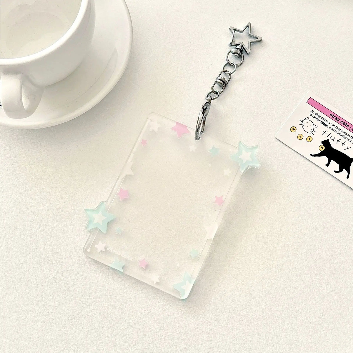 Pendentif avec porte-carte en acrylique transparent, chaîne argentée et charm à étoile sur une surface blanche.