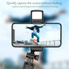 A selfie stick tripod with a fill light is positioned to capture a person jumping against a city skyline.
