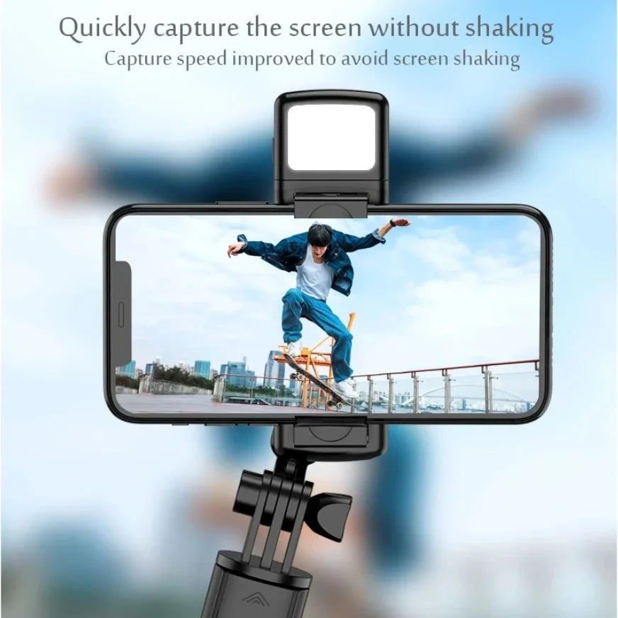 A selfie stick tripod with a fill light is positioned to capture a person jumping against a city skyline.