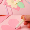 A hand is writing on a pink paper heart using a white glue pen, surrounded by various colored paper shapes.