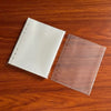 A pair of A5 transparent photo card binder sleeves, one white and one brown, resting on a wooden surface.