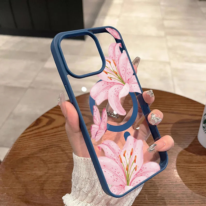 A hand holds a pink lily floral transparent iPhone case with a blue bumper on a wooden table.