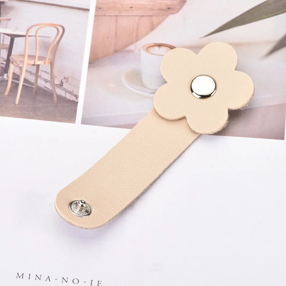 A beige leather flower cable organizer with a silver stud, shown against a light background.