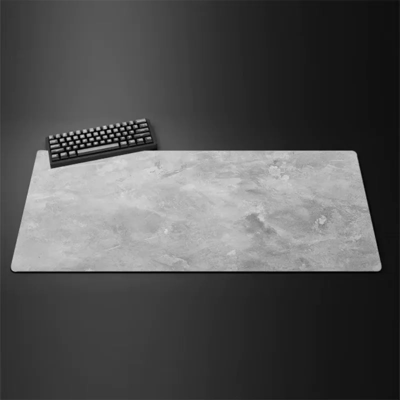 A gray overlocked mouse pad is shown next to a black computer keyboard on a dark surface.