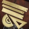 A set of brass drafting tools including rulers and triangles laid on a wooden surface.