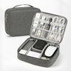 A gray travel cable organizer bag with an open compartment showing various electronic cables and accessories.