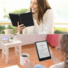 A woman is reading on a Kindle Paperwhite device in a bright indoor setting.